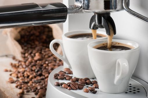Kaffekopp i en kaffemaskin ved bønner på et bord